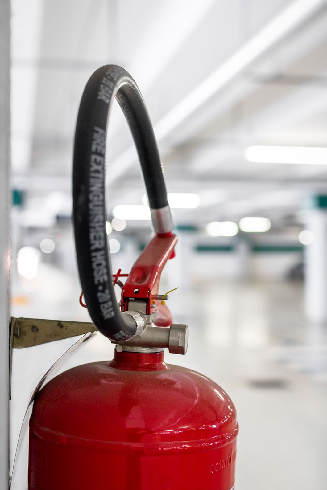 Extintor rojo con manguera negra montado en una pared blanca en un estacionamiento.