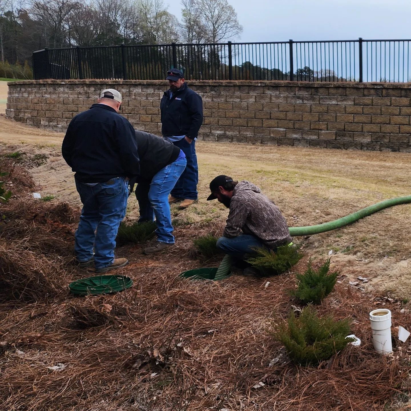 Three men working on installing irrigation pipes in a garden bed