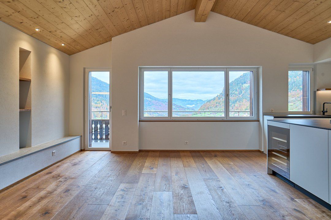 Ein leeres Wohnzimmer mit einem großen Fenster und einer Holzdecke.