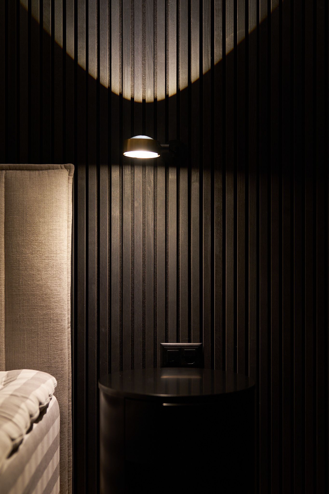 Ein Schlafzimmer mit Bett, Nachttisch, Lampe und gestreifter Wand.