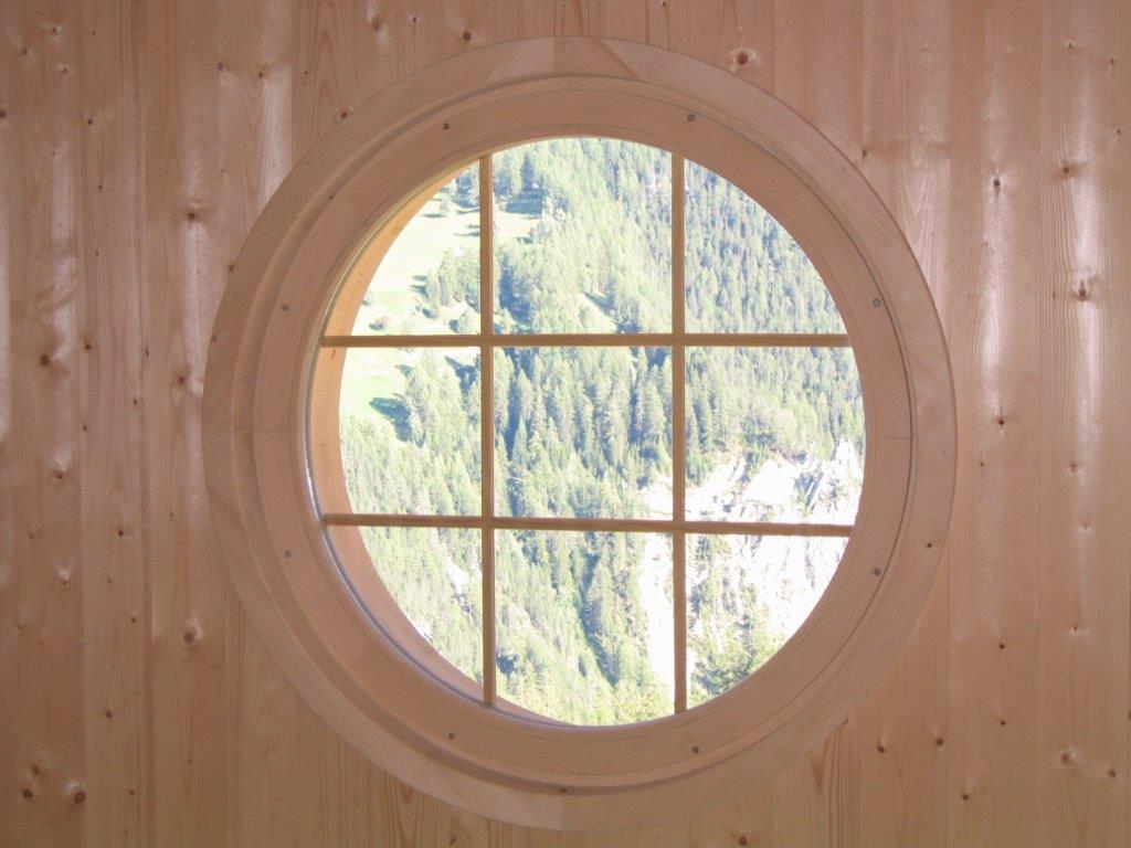 Ein rundes Fenster in einer Holzwand mit Blick auf einen Wald