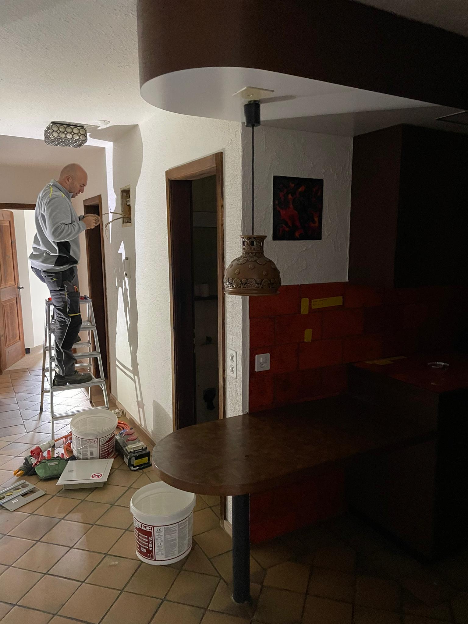 Ein Mann auf einer Leiter streicht eine Wand in einem Flur.