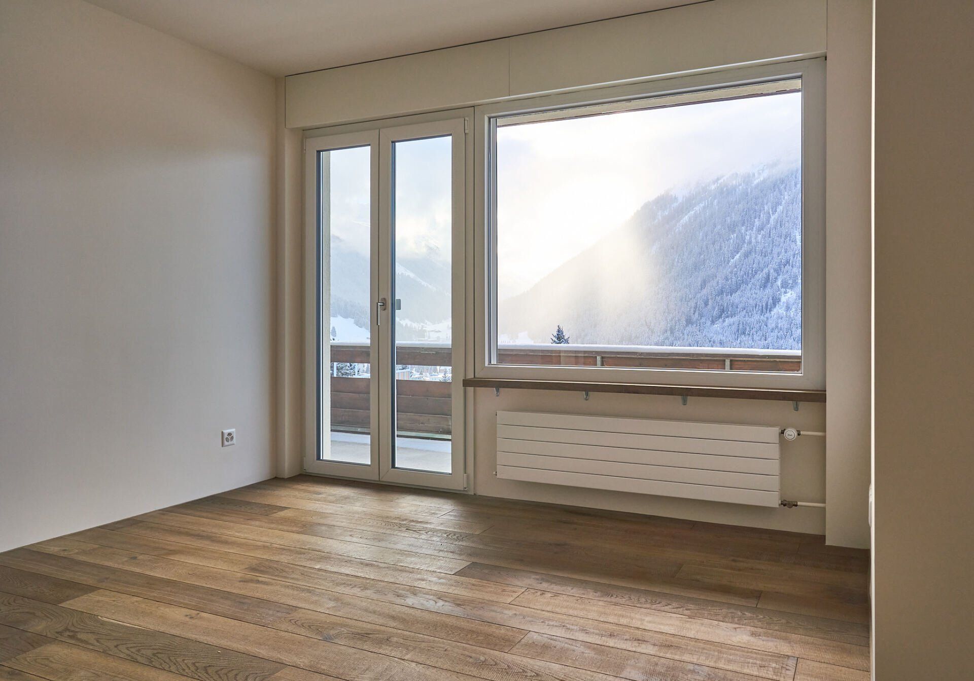 Ein leerer Raum mit einem großen Fenster und einem Holzboden.