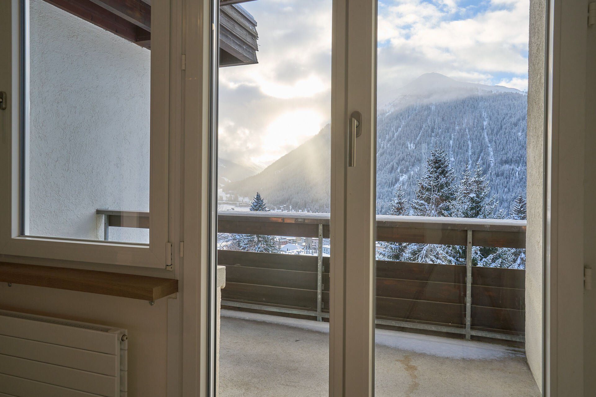Eine Glasschiebetür, die auf einen Balkon mit Bergen im Hintergrund führt.