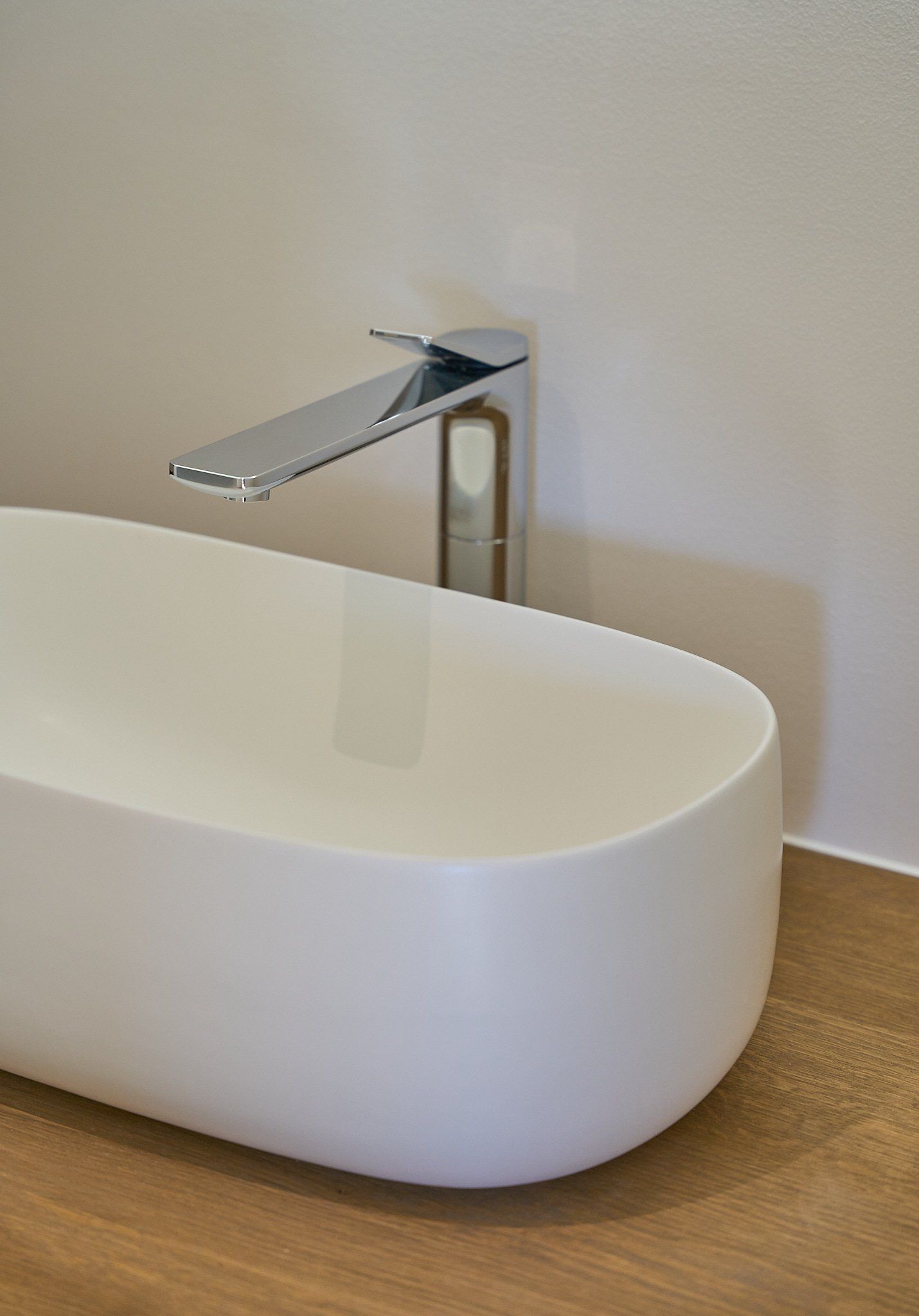 Ein weißes Waschbecken steht auf einer Holzablage in einem Badezimmer.