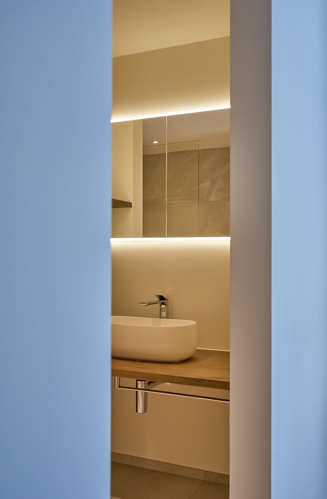 Ein Badezimmer mit einem Waschbecken und einem Spiegel hinter einer blauen Wand.