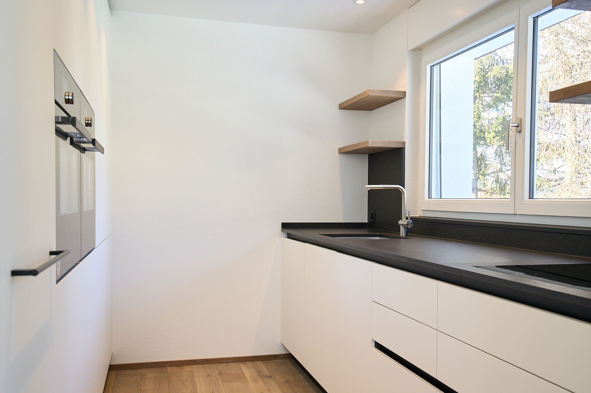 Eine Küche mit weißen Schränken und schwarzen Arbeitsplatten und einem Fenster.