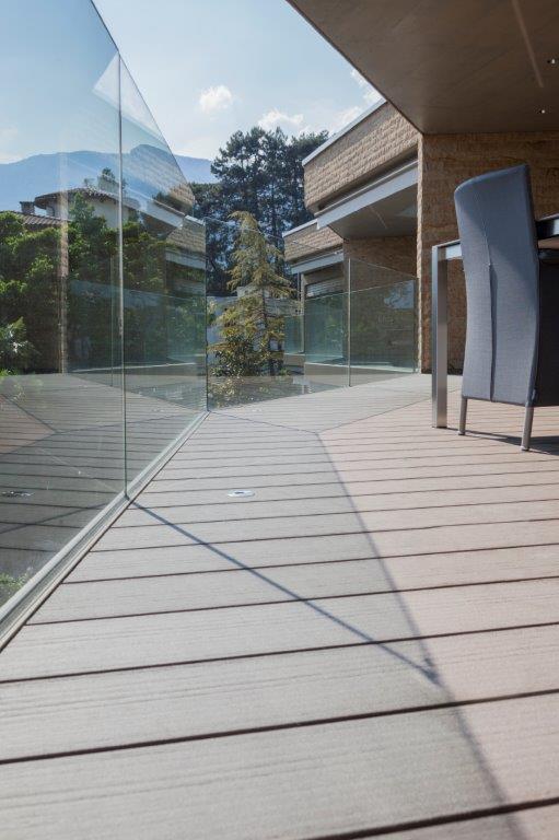 Ein Holzdeck mit Glasgeländer und einem Tisch und Stühlen darauf.