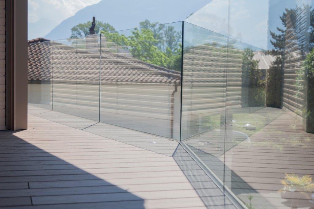 Ein Balkon mit Glasgeländer und Holzterrasse.