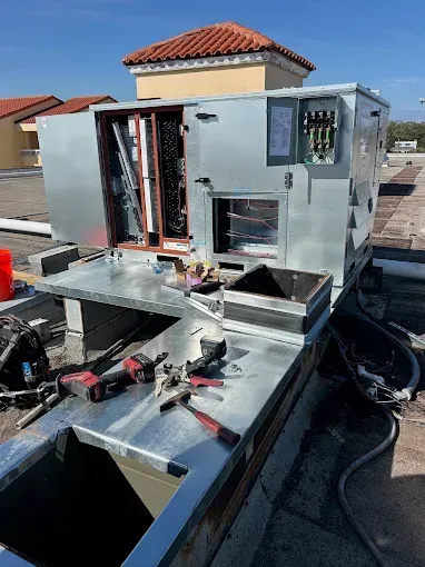 Workers repairing rooftop HVAC unit, with tools and open access panels on a flat roof.