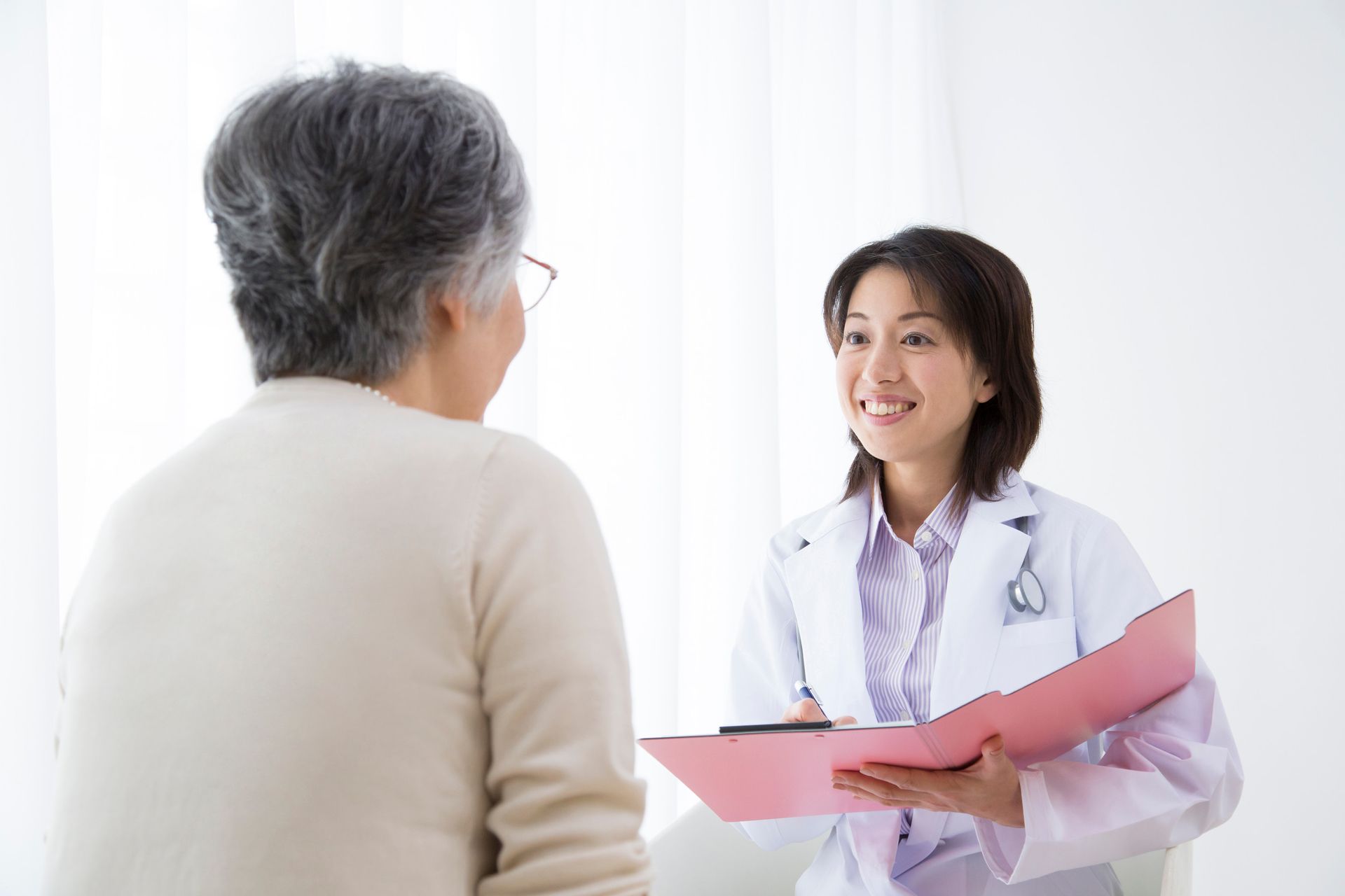 Doctor smiling at patient, holding a pink folder, in a well-lit room.