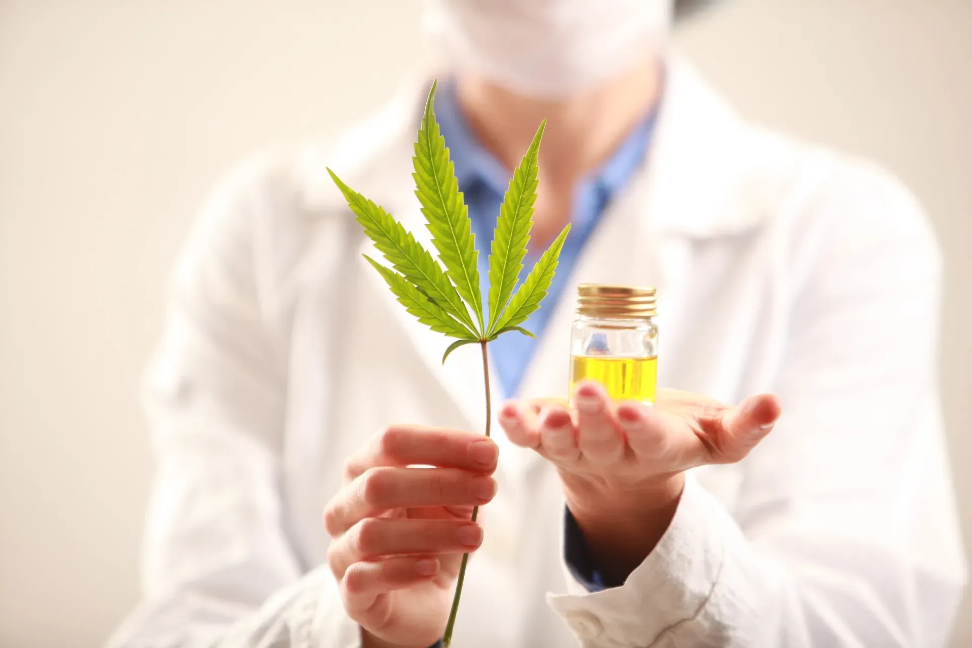 Scientist holding cannabis leaf and small jar of oil, representing research in a lab setting.