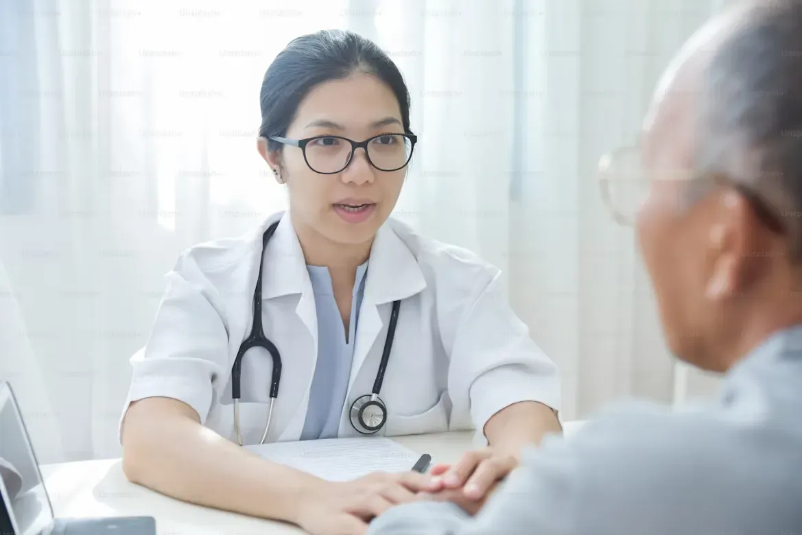 Doctor in glasses speaks with older patient in office setting.