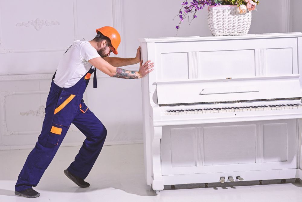 A Man in Overalls and a Hard Hat is Pushing a White Piano — Ocean Grove Removals In Whittington, VIC