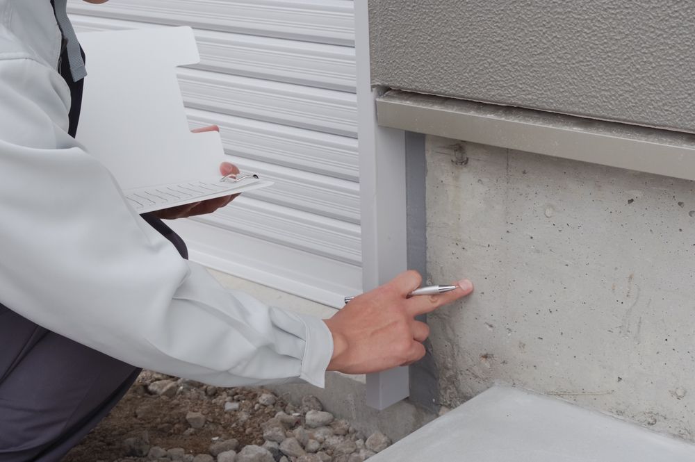 Person Inspecting a Concrete Wall for Cracks, Holding a Clipboard and Pen — Pioneer Pest Mackay In Glenella, QLD