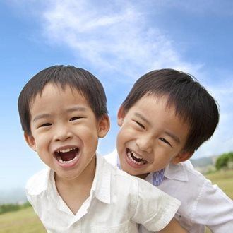 Two smiling children in white shirts against a blue sky, one with arms around the other.