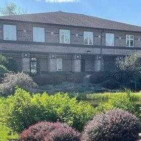 Two-story brick building with multiple windows, surrounded by green shrubbery.