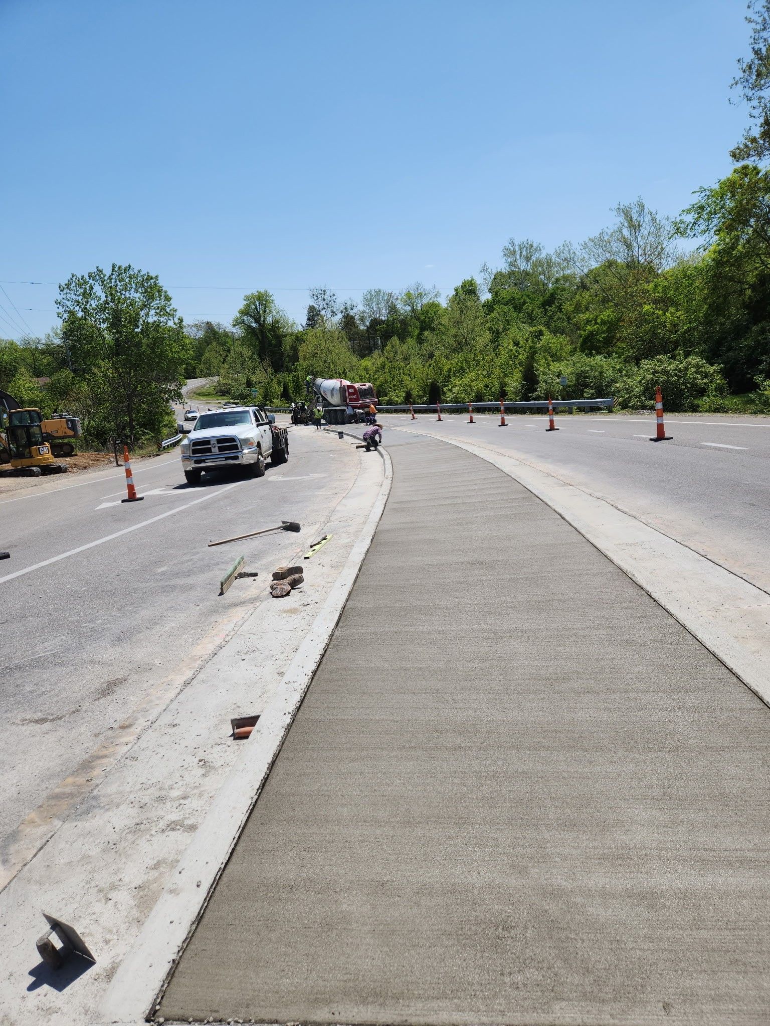 Road construction; a newly paved lane with a car and truck approaching under a blue sky, lined with cones.