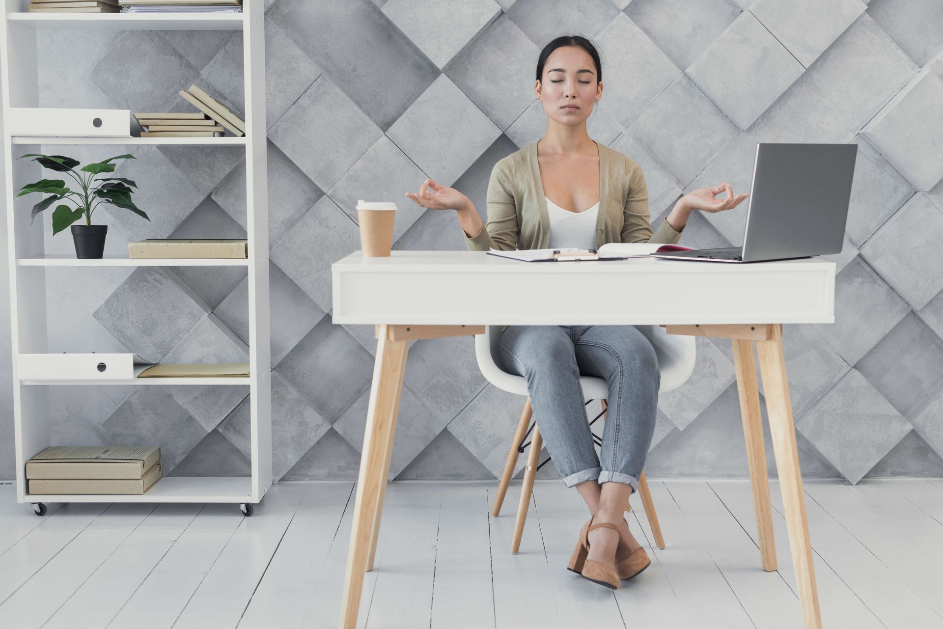 Une femme assise à un bureau médite devant un ordinateur portable
