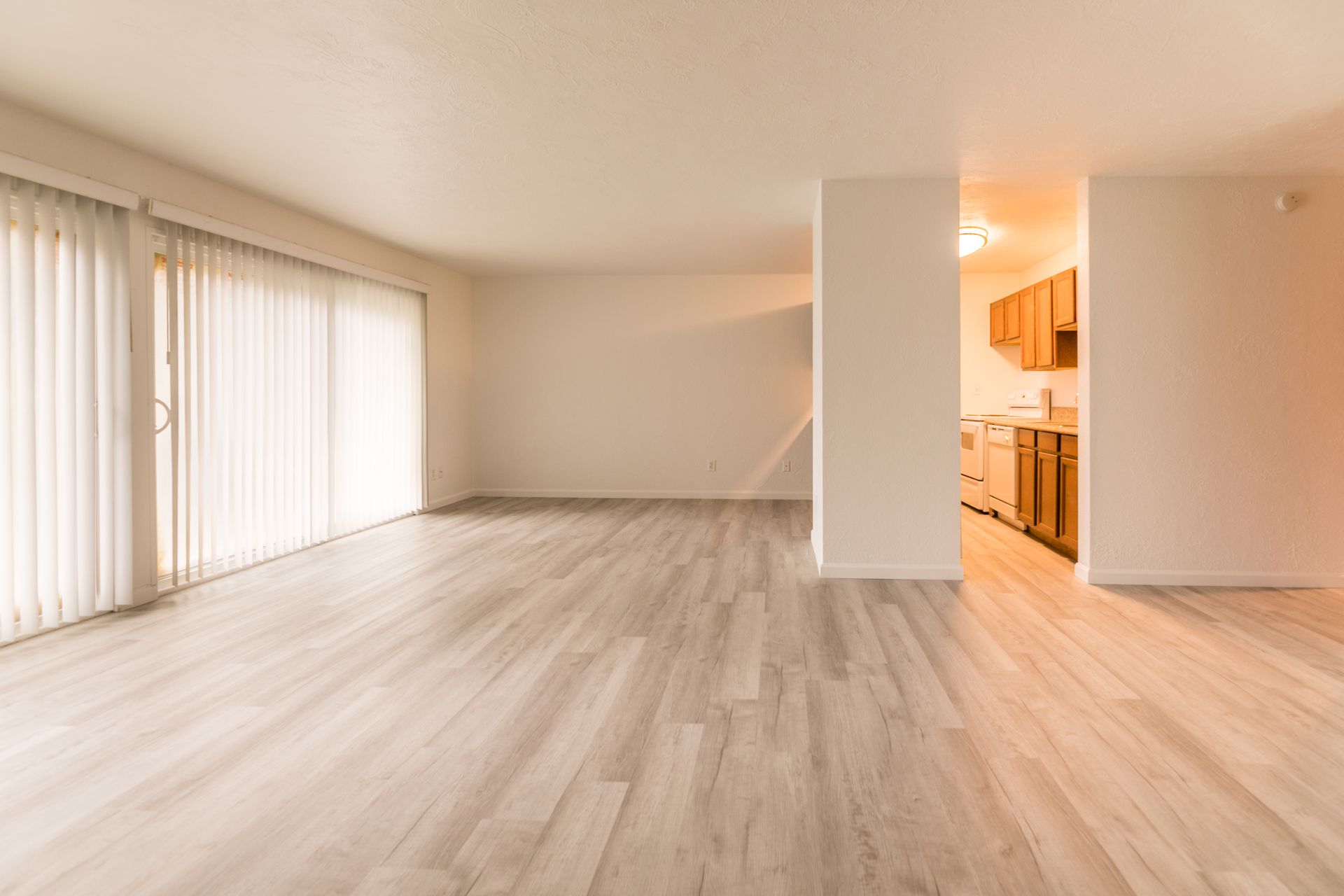 An empty living room with hardwood floors and sliding glass doors leading to a kitchen.