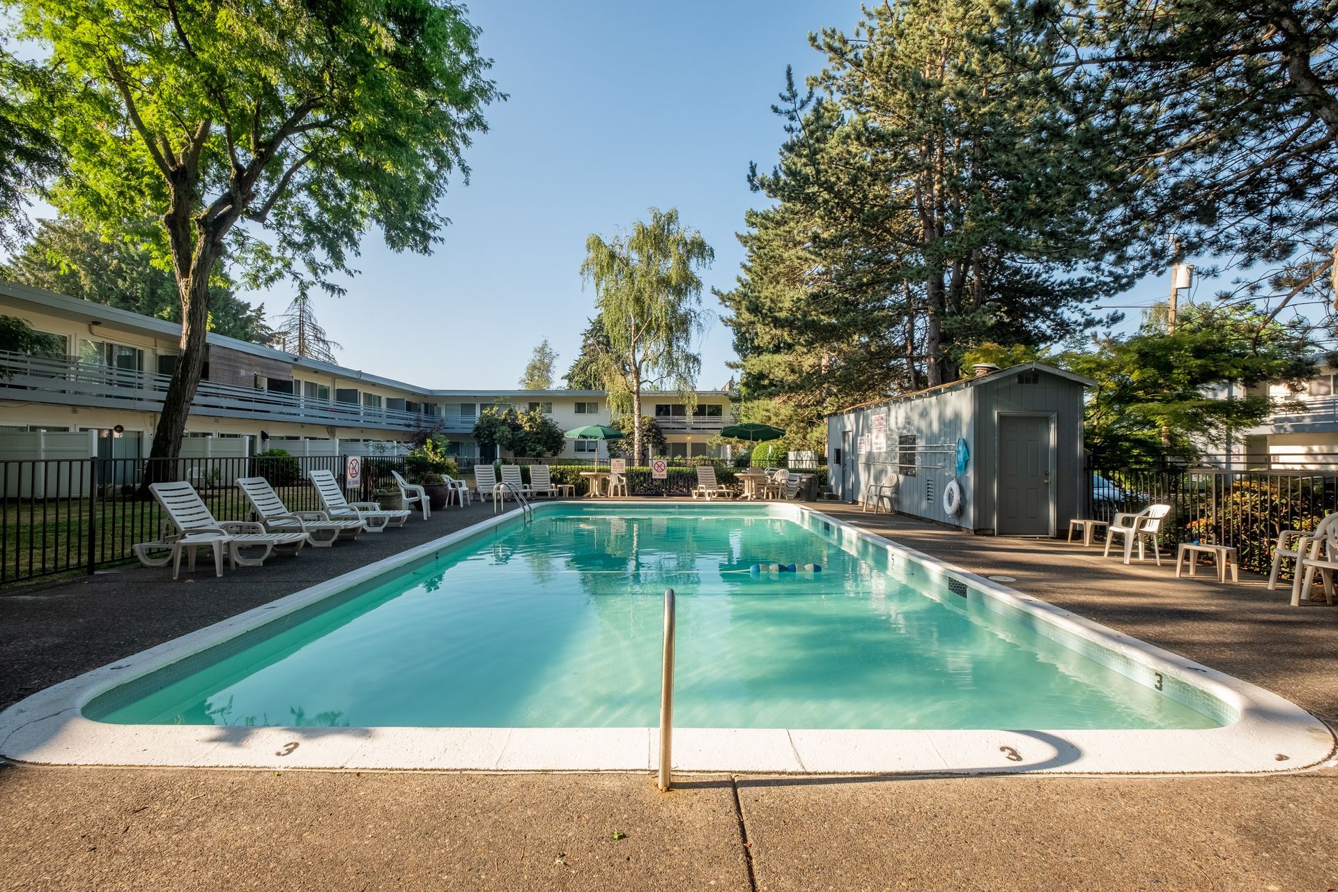 A large swimming pool surrounded by chairs and trees in front of a building.