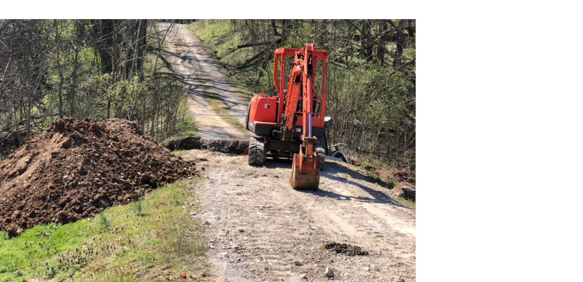 A red excavator is driving down a dirt road.