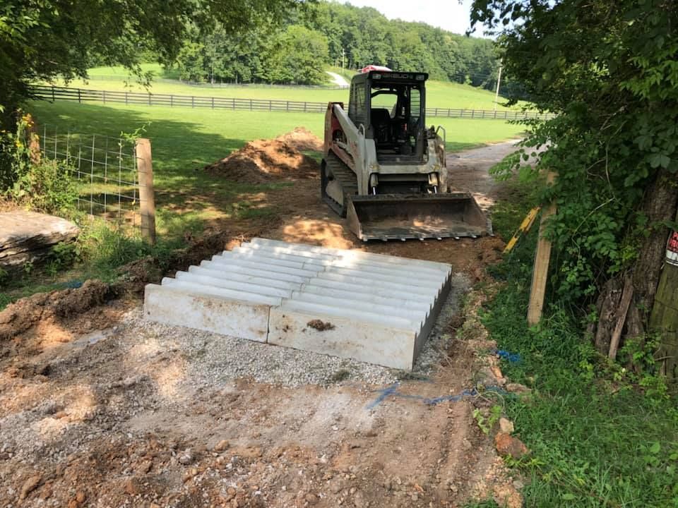 A bulldozer is driving down a dirt road next to a field.