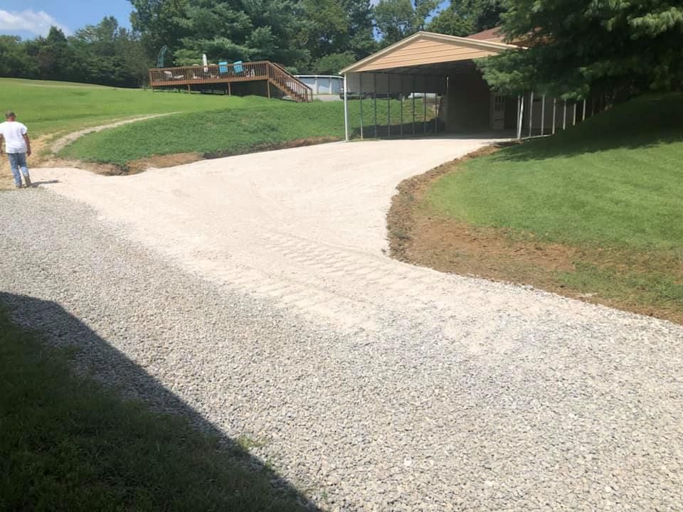 A man is walking down a gravel driveway towards a house.