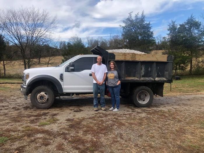 A man and a woman are standing in front of a dump truck.