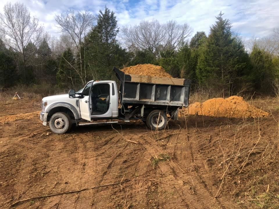 A dump truck is sitting in the middle of a dirt field.