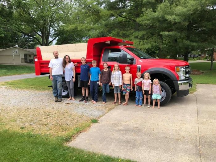 A group of people standing in front of a red dump truck.