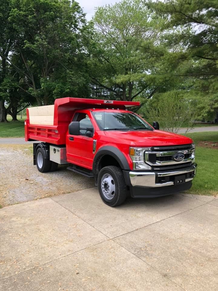 A red dump truck is parked in a driveway next to trees.