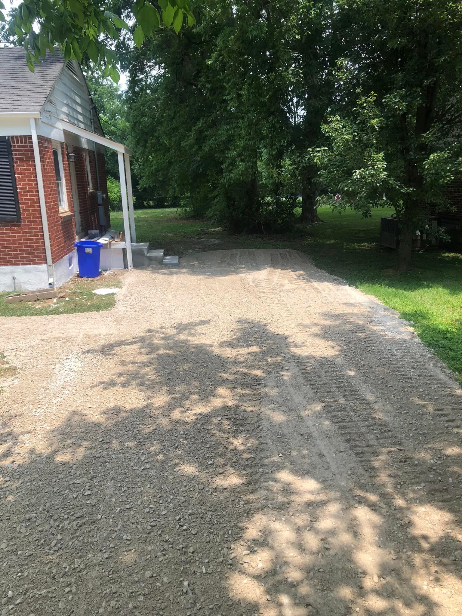 A gravel driveway leading to a brick house surrounded by trees.