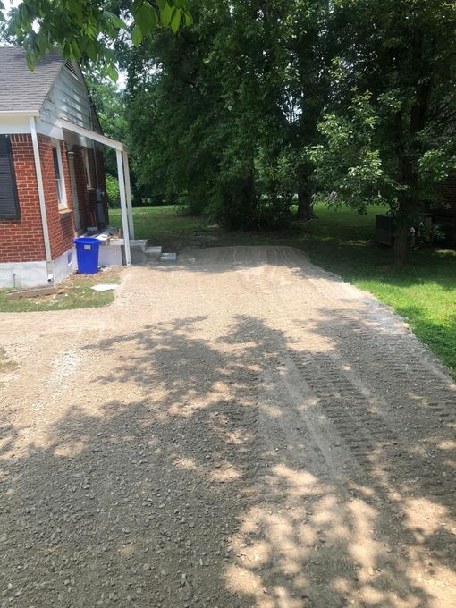 A gravel driveway leading to a brick house surrounded by trees.