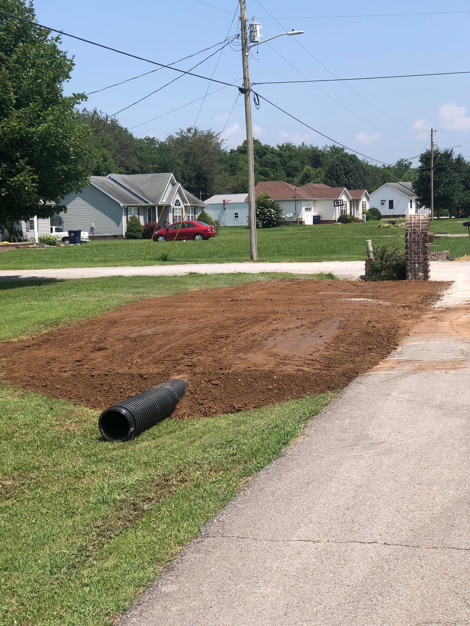 A black pipe is laying in the grass next to a road.