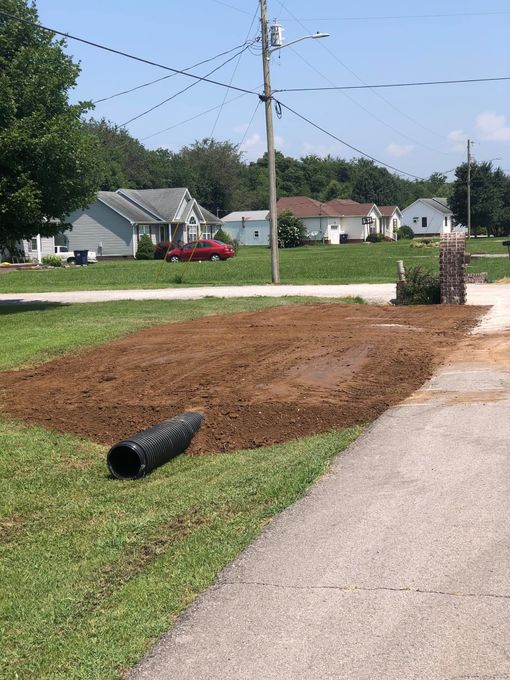 A black pipe is laying in the grass next to a road.