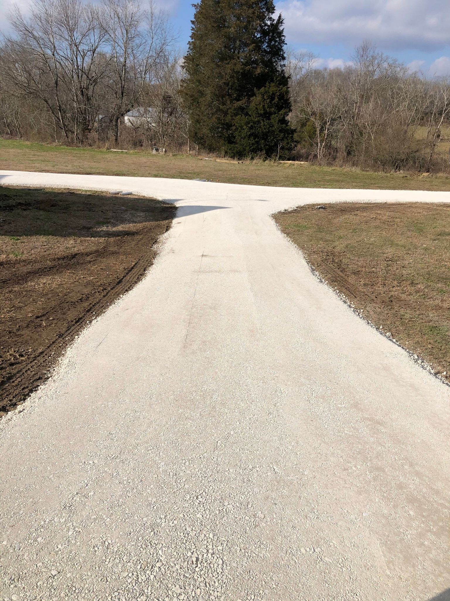 A gravel road going through a field with trees in the background.