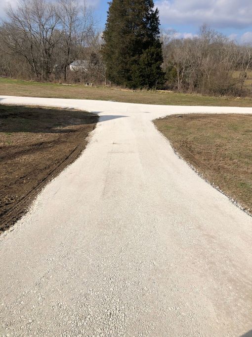 A gravel road going through a field with trees in the background.