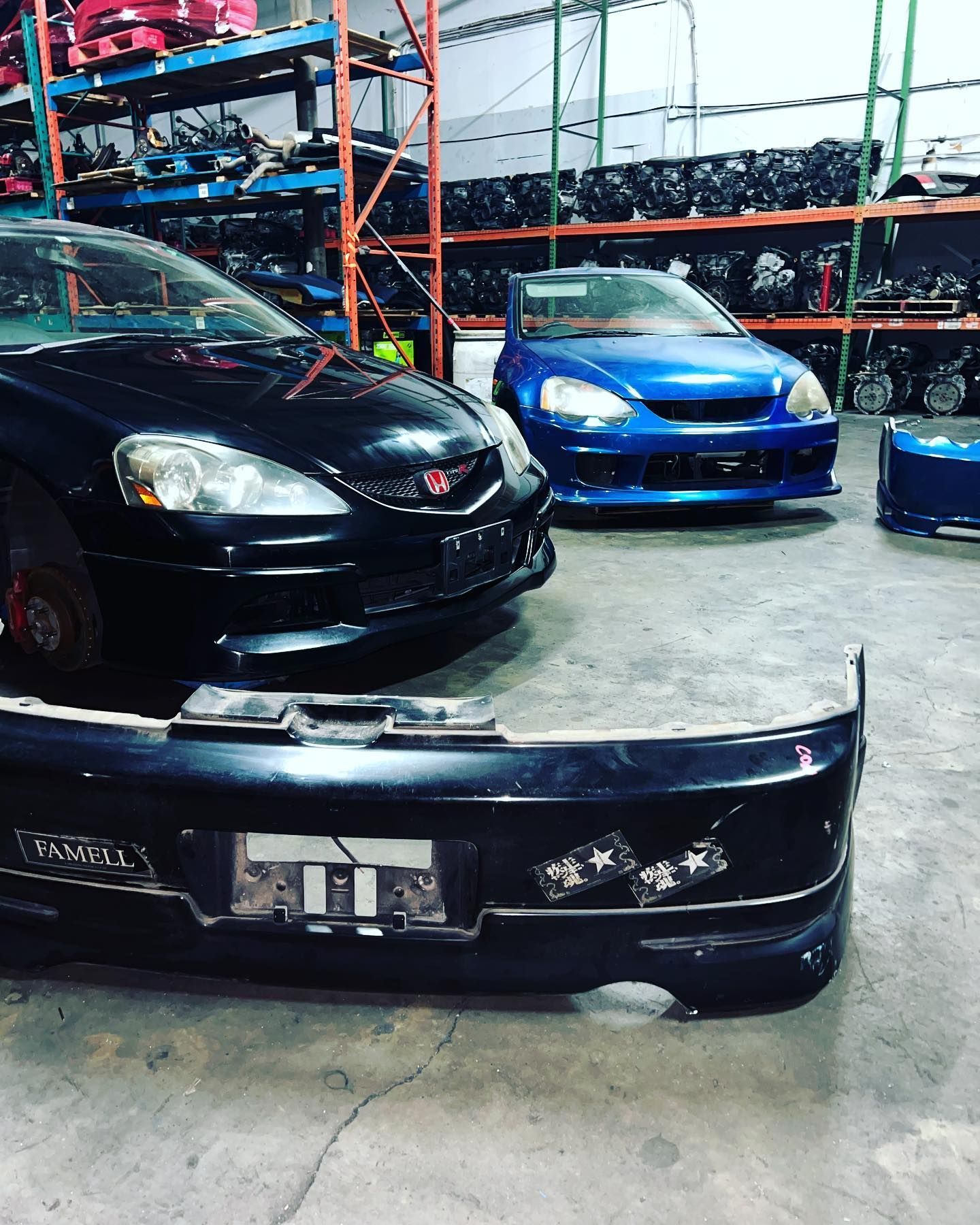 Two Honda Integra/RSX coupes, one black and one blue, parked in an auto parts warehouse