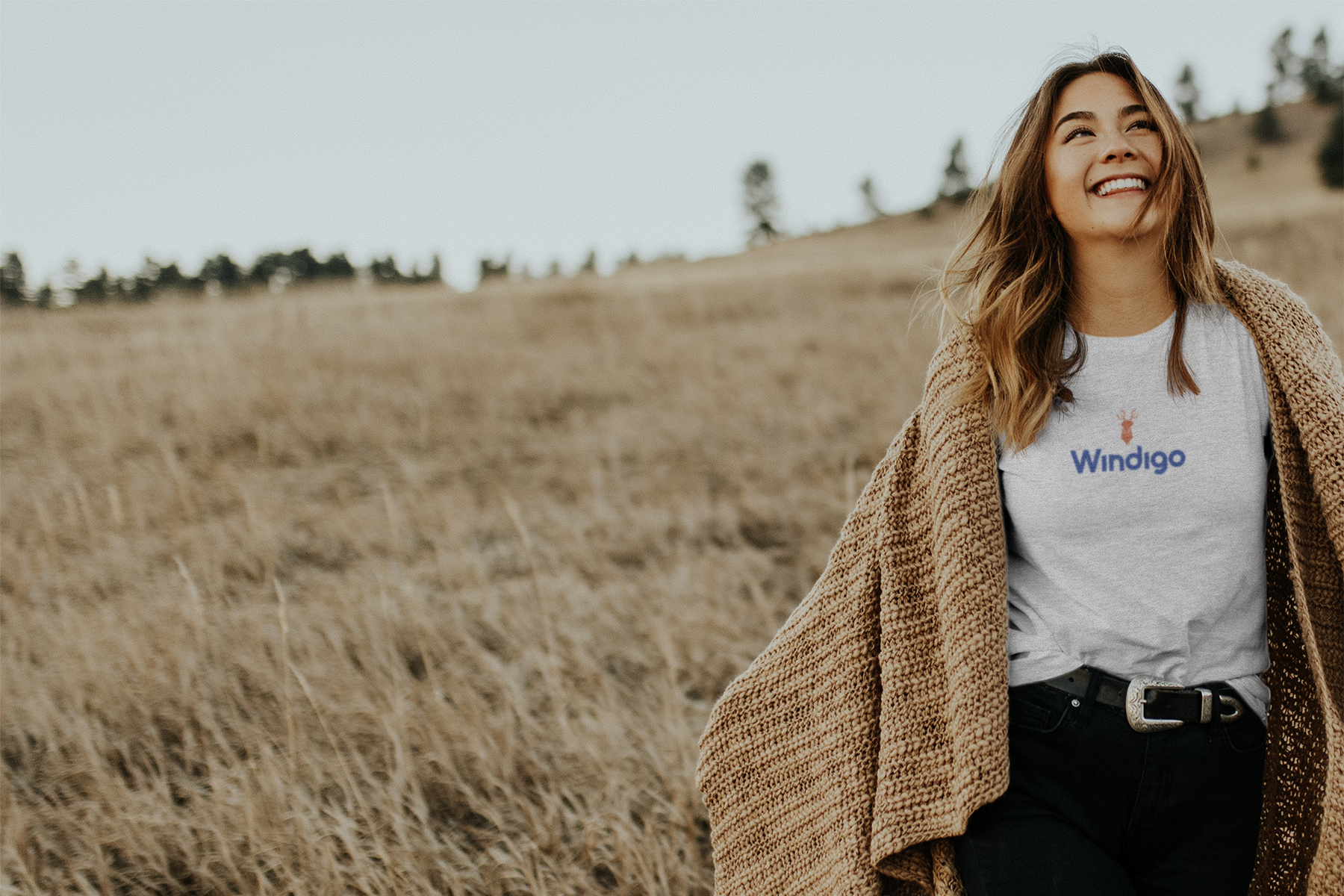 Een vrouw lacht terwijl ze in een veld loopt, gekleed in een trui en een T-shirt met het 