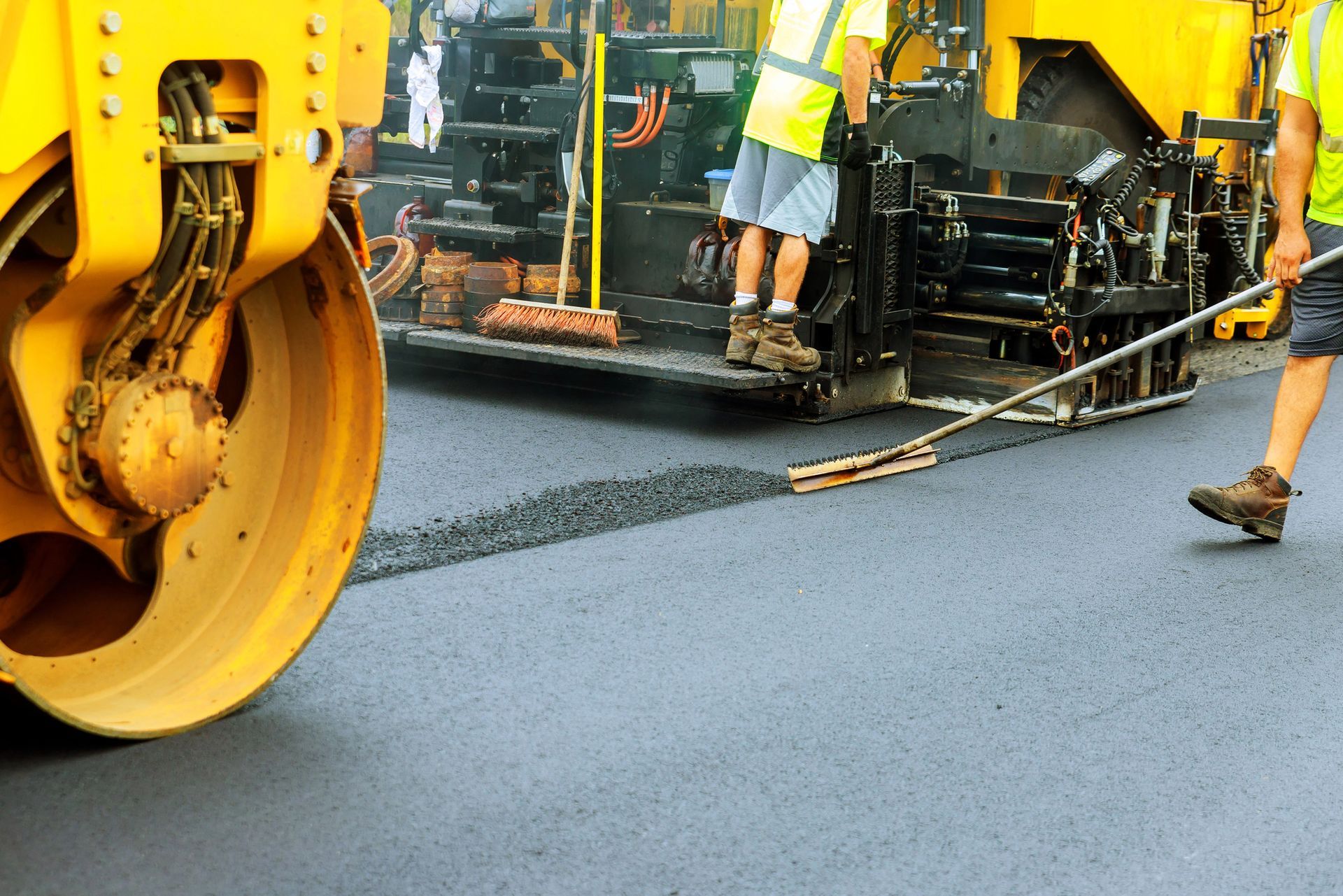 Gli operai utilizzano macchinari per pavimentare una strada con asfalto fresco e scuro.