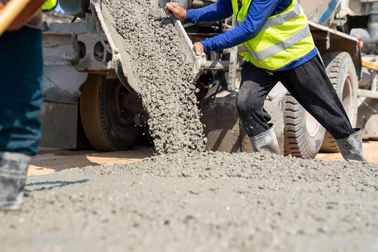 Un operaio con indosso un giubbotto ad alta visibilità guida il getto di calcestruzzo fresco dallo scivolo di un camion in un cantiere.