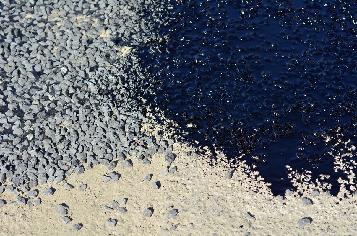 Una vista dall'alto che mostra la transizione da ghiaia grigia e sciolta sulla sinistra a una zona di asfalto scuro e lucido sulla destra.