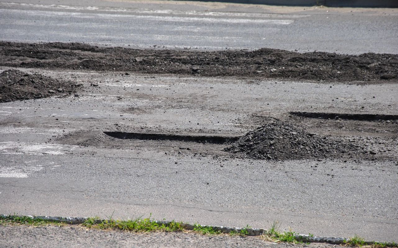 Una superficie stradale asfaltata con diverse buche profonde e scure e cumuli di ghiaia smossa sparsi su tutta la superficie.