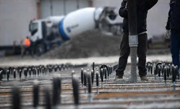 Operai edili versano cemento su una fondazione con barre d'armatura di supporto e una betoniera sullo sfondo.