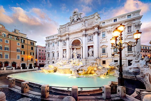 Fontana de Trevi en Roma, Italia, al atardecer. Fuente de mármol blanco con figuras y agua de color turquesa brillante.