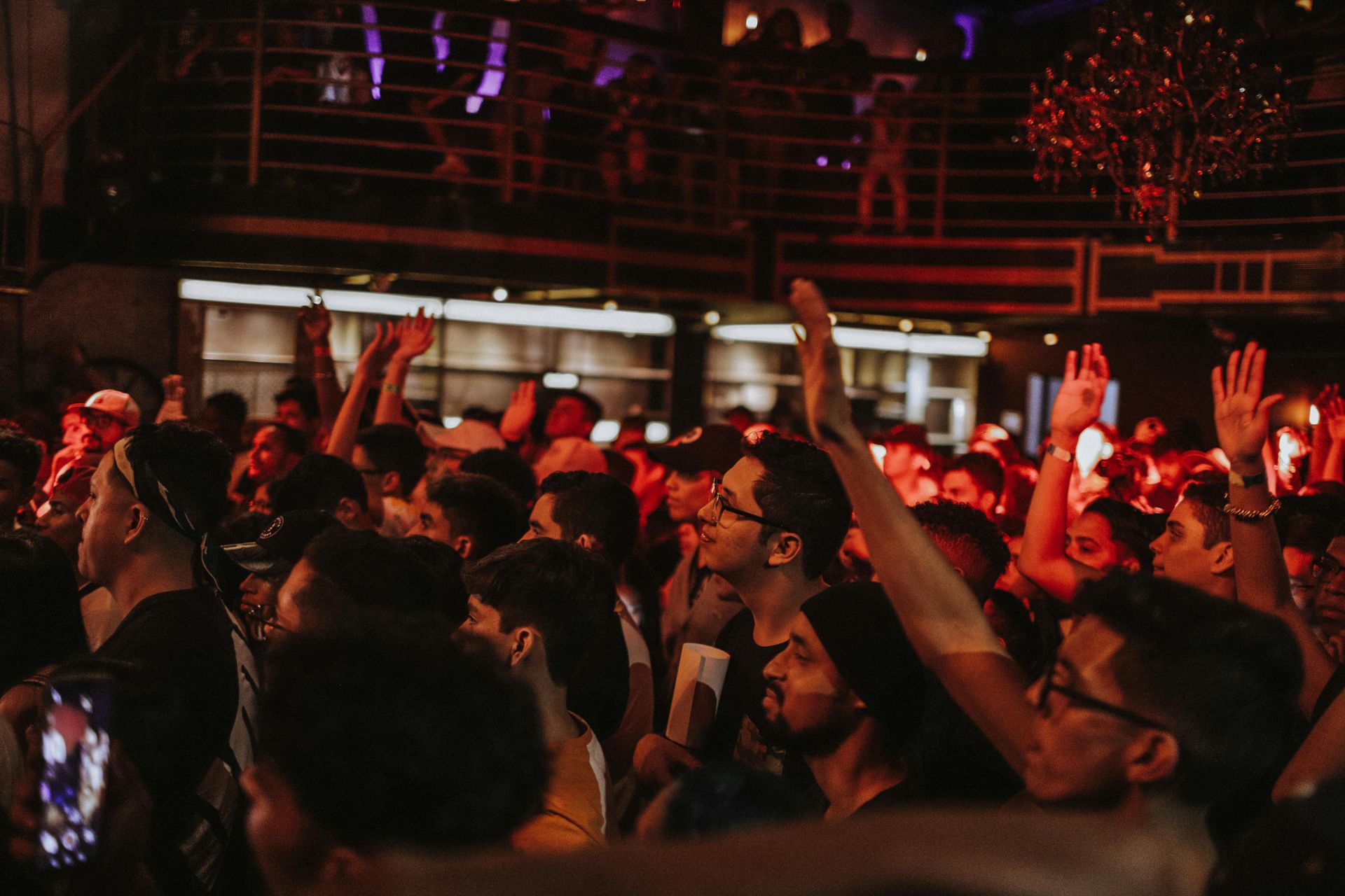 Crowd in a dimly lit club with raised arms, enjoying the music. Red and purple lighting.
