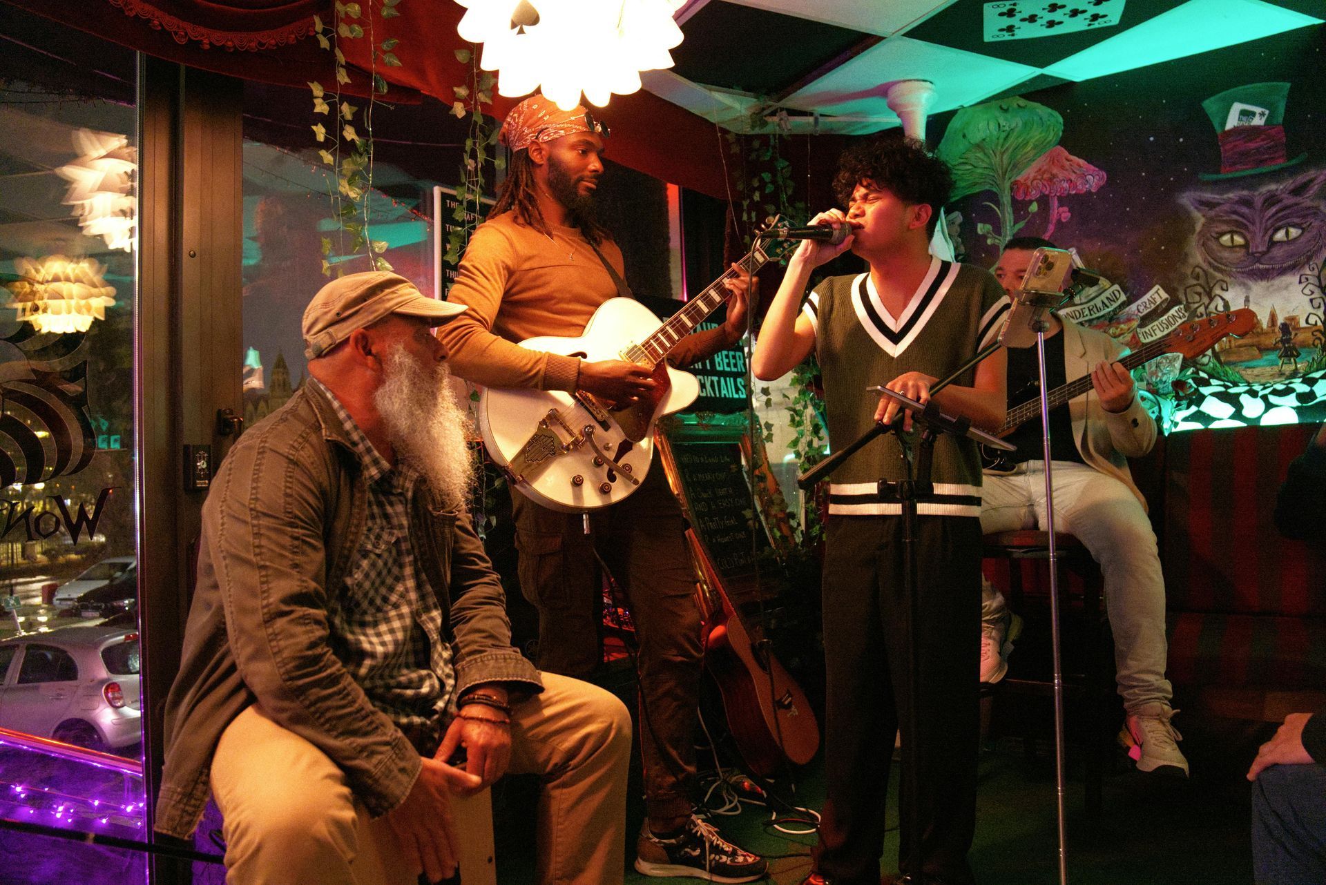 A band performs in a whimsical venue. Two guitarists and a singer. A person seated listens.