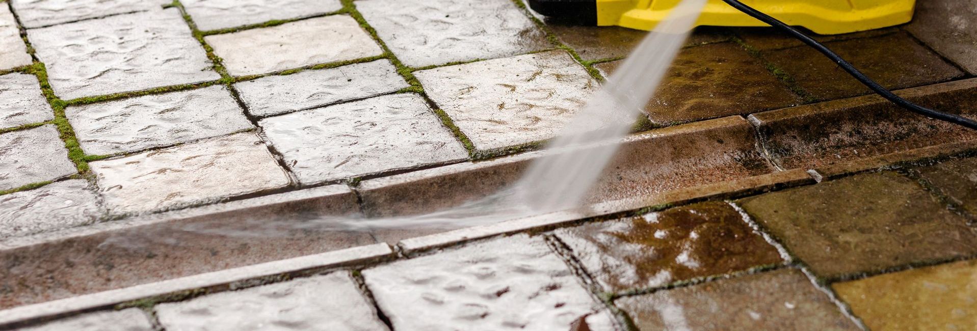 Power washer cleaning a brick patio; water spraying.