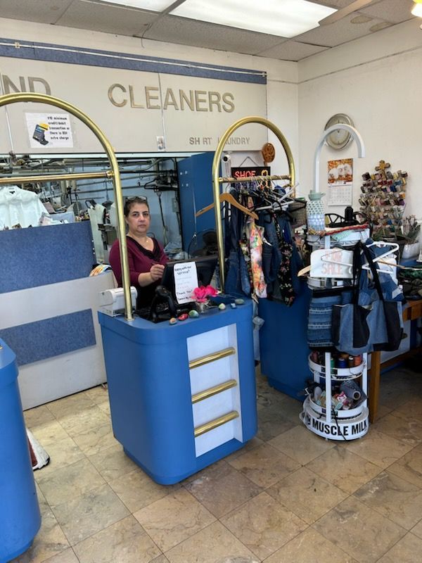 Woman stands behind a blue counter in a dry cleaner.